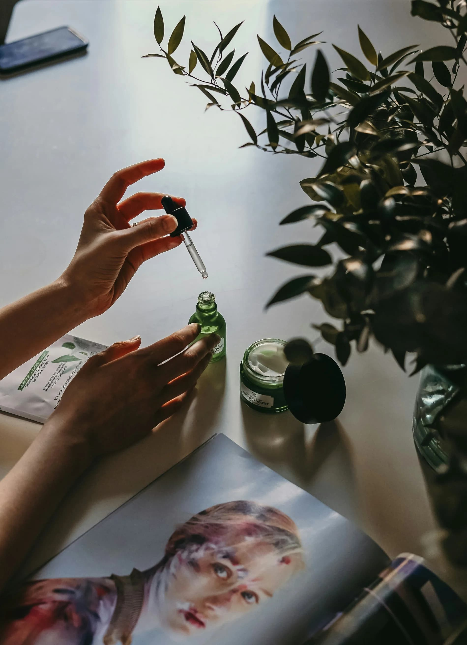 Hand holding a dropper bottle above botanical skincare